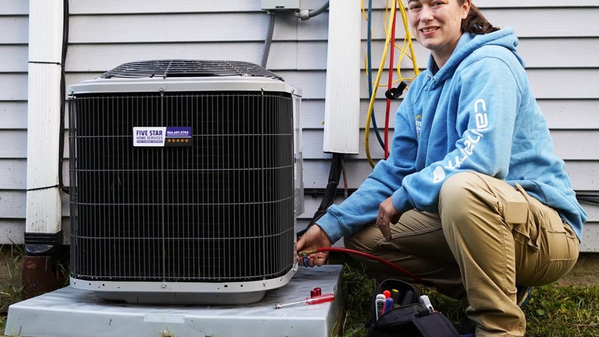 Technician with gauges servicing an outdoor AC condenser beside a home