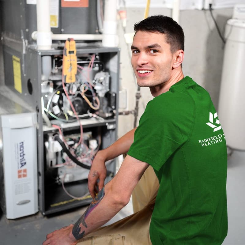 Smiling technician in green shirt beside open furnace